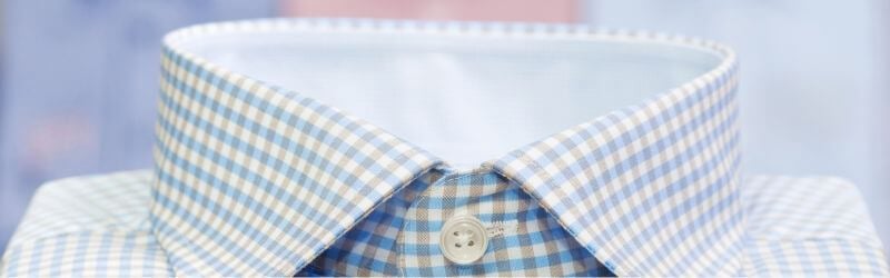 Primer plano de una camisa de vestir a cuadros azules y blancos pulcramente planchada con cuello abotonado.