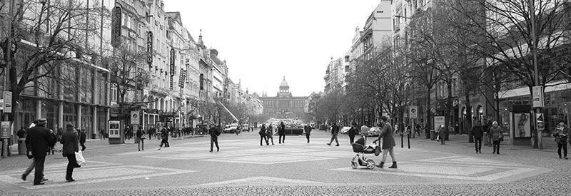 Una amplia calle peatonal bordeada de árboles y edificios, con gente paseando y un edificio abovedado a lo lejos.