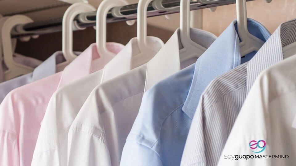 Varias camisas de vestir pulcramente planchadas en tonos blancos, rosas y azules cuelgan de perchas en un armario.