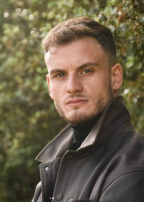 Roberto Zonato mira a la cámara, su cabello corto y su barba recortada complementan perfectamente la exuberante vegetación detrás de él.